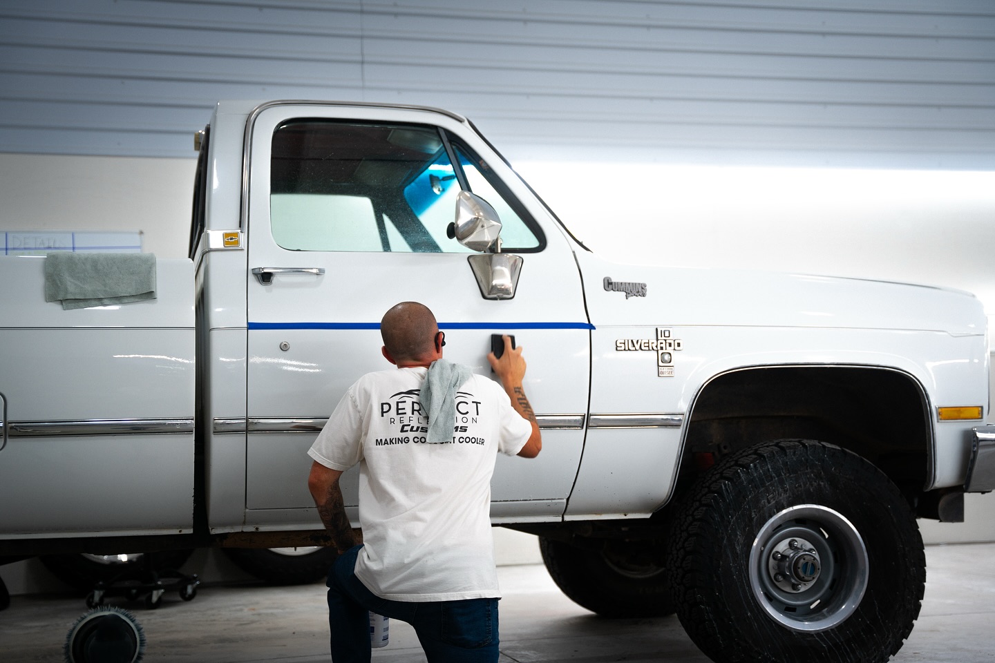 Technician wet sanding a white Chevrolet Silverado during refinishing